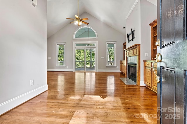 unfurnished living room featuring hardwood / wood-style floors, ceiling fan, high vaulted ceiling, and a tiled fireplace