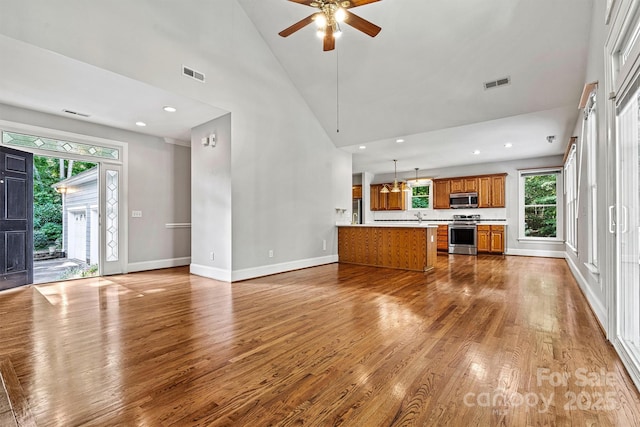 unfurnished living room featuring a wealth of natural light, high vaulted ceiling, wood-type flooring, and ceiling fan