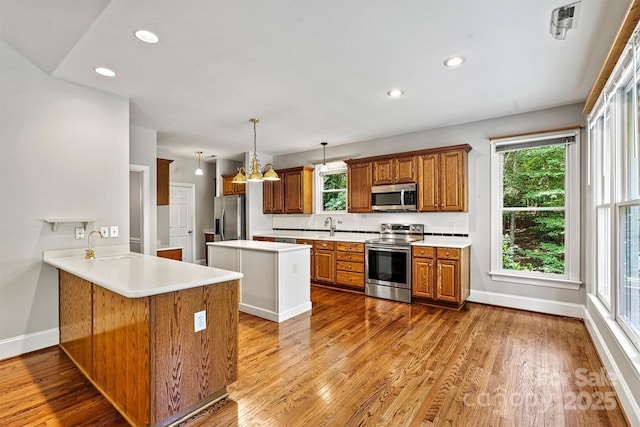 kitchen with pendant lighting, appliances with stainless steel finishes, a notable chandelier, light hardwood / wood-style floors, and kitchen peninsula