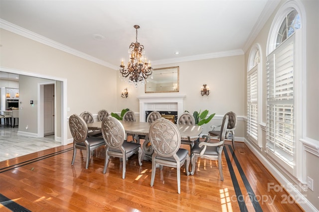 dining space featuring a tile fireplace, ornamental molding, a chandelier, and light wood-type flooring