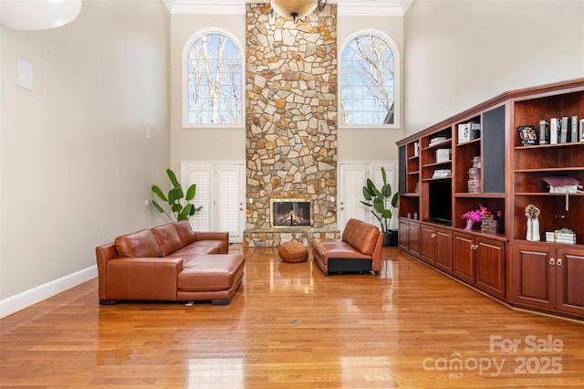 living room with a high ceiling, a stone fireplace, ornamental molding, and light hardwood / wood-style flooring