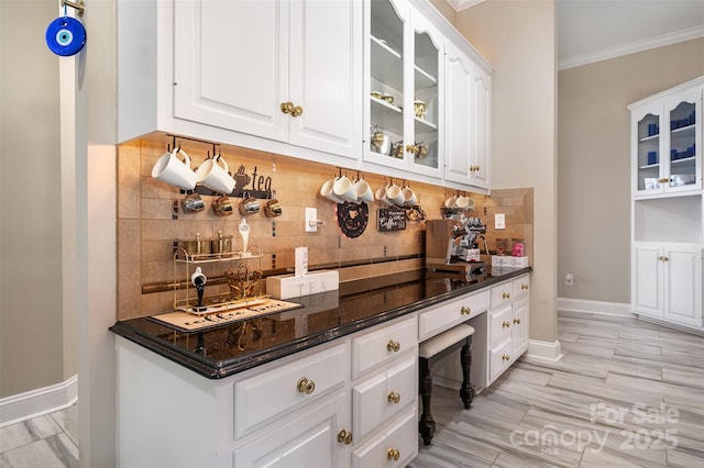 bar featuring white cabinets, decorative backsplash, dark stone counters, and ornamental molding