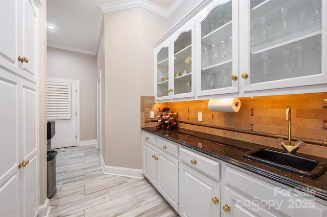 bar with tasteful backsplash, dark stone countertops, crown molding, white cabinets, and sink