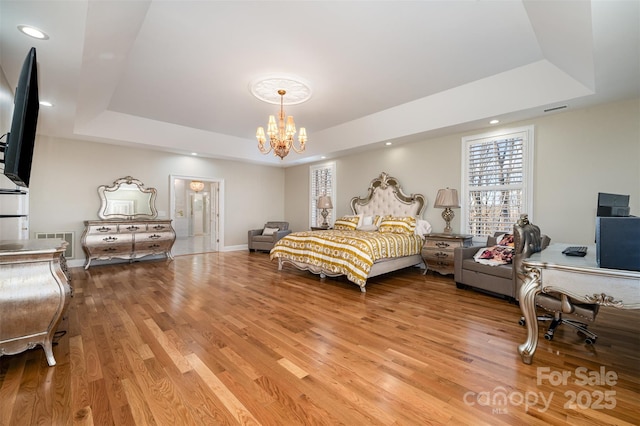 bedroom featuring light hardwood / wood-style floors, a tray ceiling, and a notable chandelier