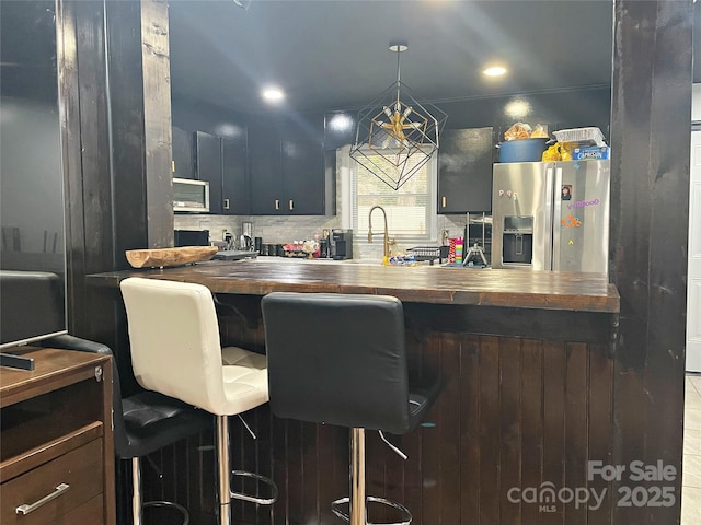 kitchen featuring wood counters, stainless steel fridge with ice dispenser, a breakfast bar, and pendant lighting