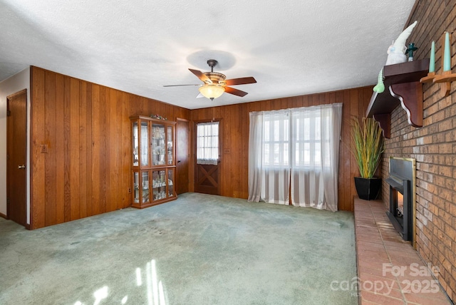 unfurnished living room featuring a textured ceiling, ceiling fan, carpet flooring, and wooden walls