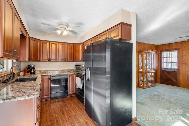 kitchen with sink, wooden walls, ceiling fan, light stone countertops, and black appliances