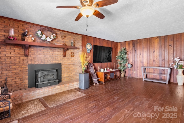 living room featuring a textured ceiling, wood walls, ceiling fan, and a wood stove