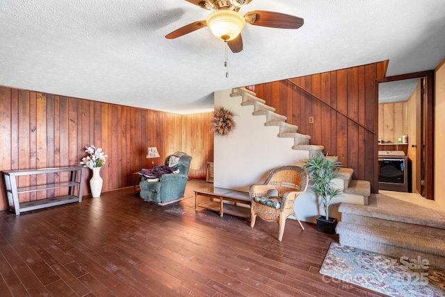 living area featuring washer / dryer, wood walls, ceiling fan, and dark wood-type flooring