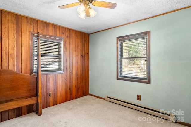 empty room featuring baseboard heating, wood walls, light colored carpet, ceiling fan, and a textured ceiling