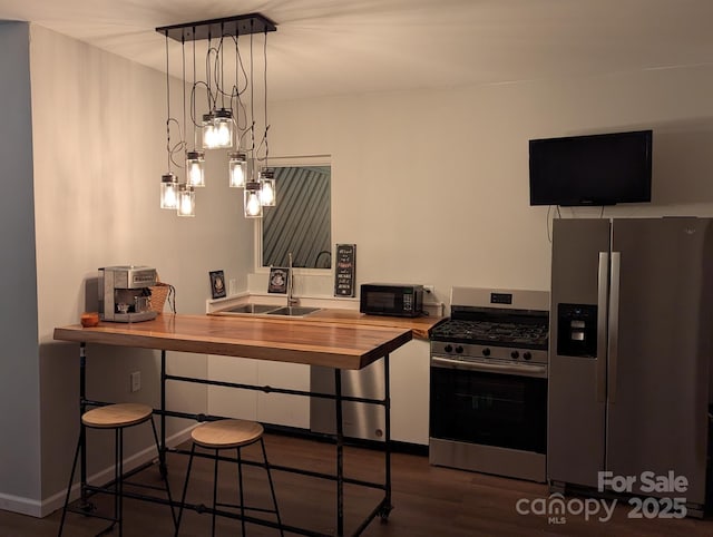 kitchen featuring sink, wooden counters, appliances with stainless steel finishes, white cabinets, and decorative light fixtures