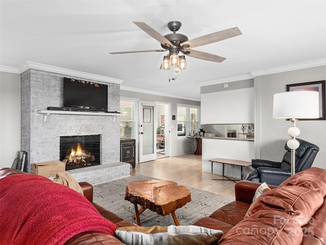 living room featuring ornamental molding, a ceiling fan, a brick fireplace, and wood finished floors