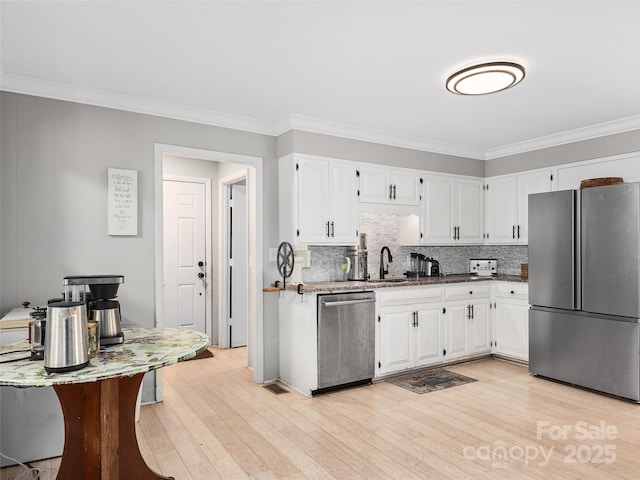 kitchen with light wood finished floors, appliances with stainless steel finishes, ornamental molding, and white cabinetry