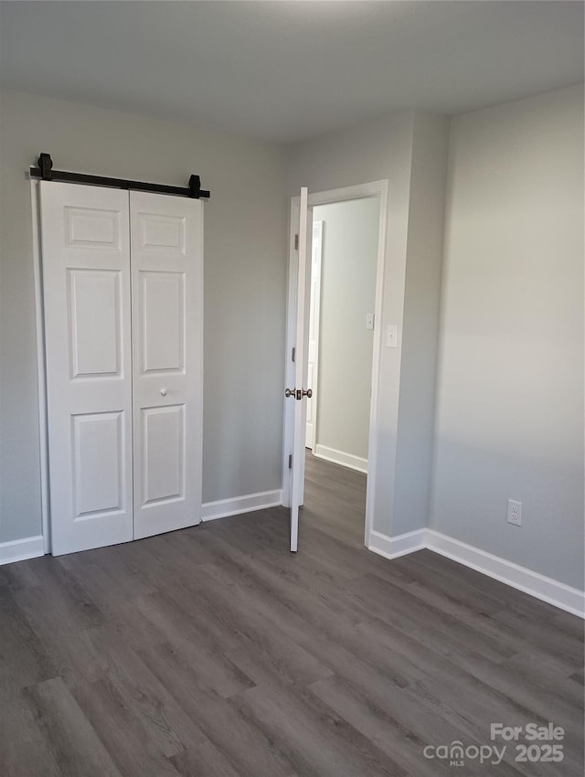 unfurnished bedroom with dark hardwood / wood-style flooring, a closet, and a barn door