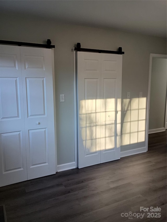 unfurnished bedroom with dark hardwood / wood-style floors and a barn door