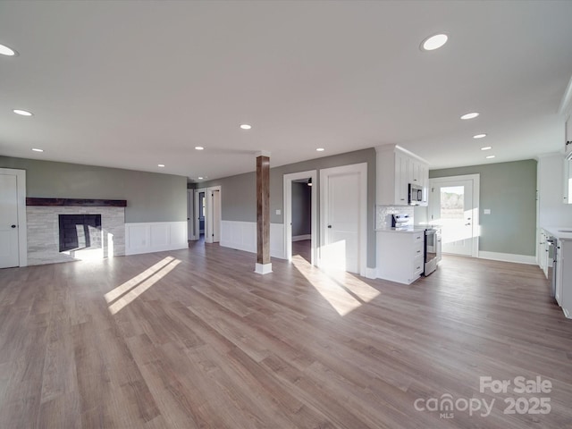 unfurnished living room featuring decorative columns, a fireplace, and light hardwood / wood-style flooring