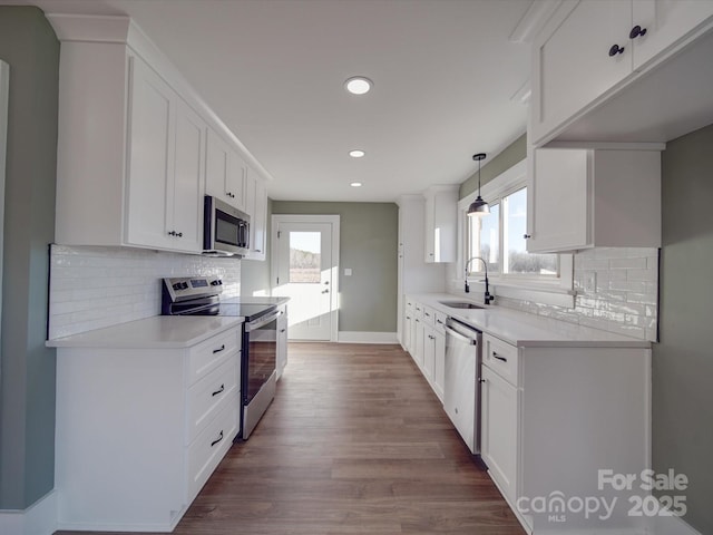 kitchen featuring stainless steel appliances, sink, wood-type flooring, white cabinets, and hanging light fixtures