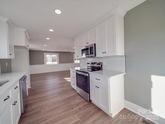 kitchen featuring appliances with stainless steel finishes, light wood-type flooring, tasteful backsplash, and white cabinetry