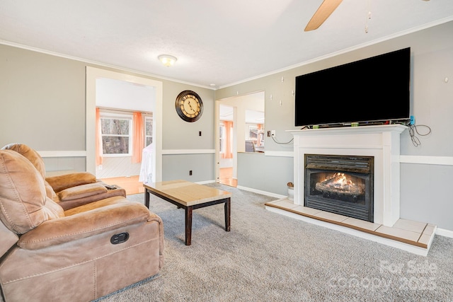 carpeted living room with ceiling fan, crown molding, and a tile fireplace