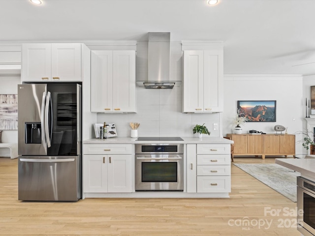 kitchen with stainless steel appliances, wall chimney range hood, backsplash, and white cabinetry