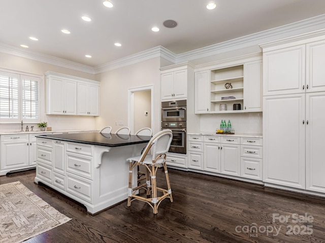 kitchen featuring double oven, dark hardwood / wood-style flooring, white cabinetry, and a kitchen bar