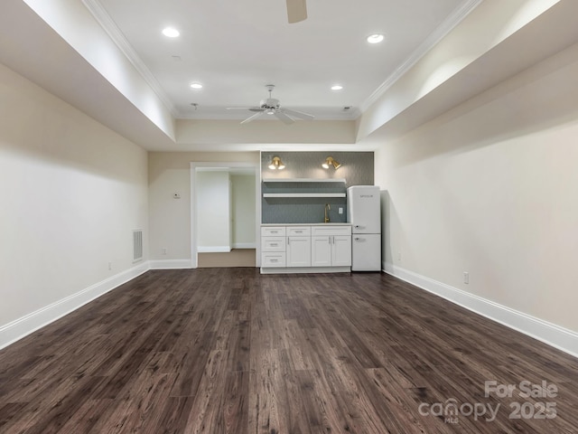 unfurnished living room with ceiling fan, dark hardwood / wood-style floors, sink, crown molding, and a tray ceiling