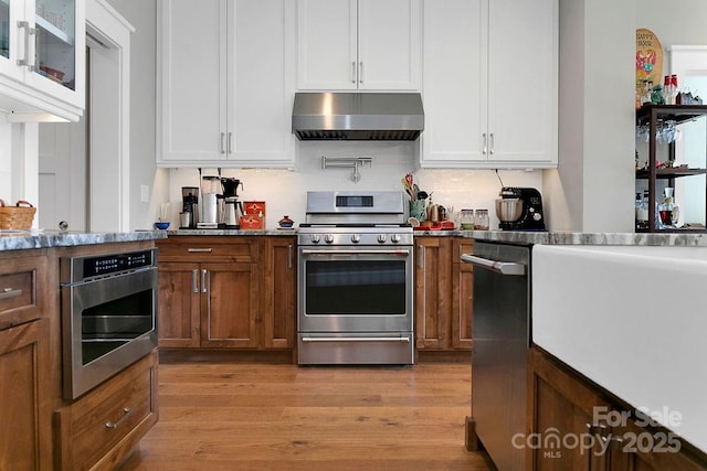 kitchen with stainless steel appliances, extractor fan, white cabinets, and light hardwood / wood-style floors