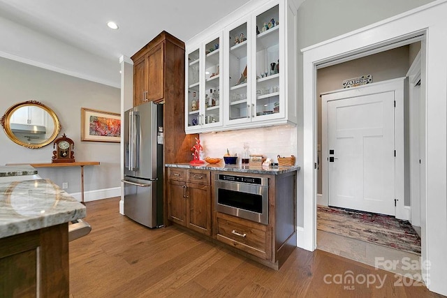 kitchen with light stone countertops, decorative backsplash, wood-type flooring, and stainless steel appliances