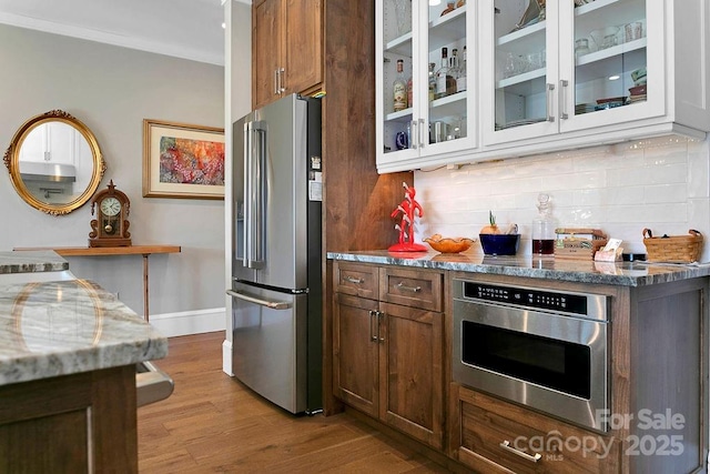 kitchen with high end fridge, dark stone countertops, wall oven, tasteful backsplash, and light wood-type flooring