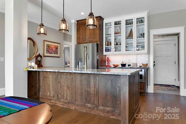 kitchen with light stone counters, decorative light fixtures, high quality fridge, kitchen peninsula, and backsplash