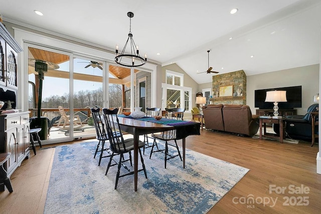 dining space with ceiling fan with notable chandelier, lofted ceiling, and light hardwood / wood-style floors