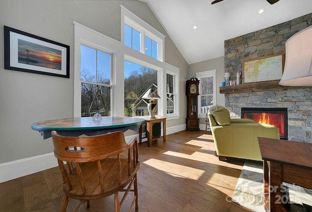 dining area featuring a stone fireplace, wood-type flooring, ceiling fan, and vaulted ceiling