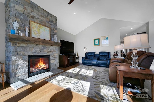 living room featuring lofted ceiling, hardwood / wood-style flooring, a stone fireplace, and ceiling fan