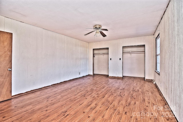 unfurnished bedroom with light wood-type flooring, two closets, and ceiling fan