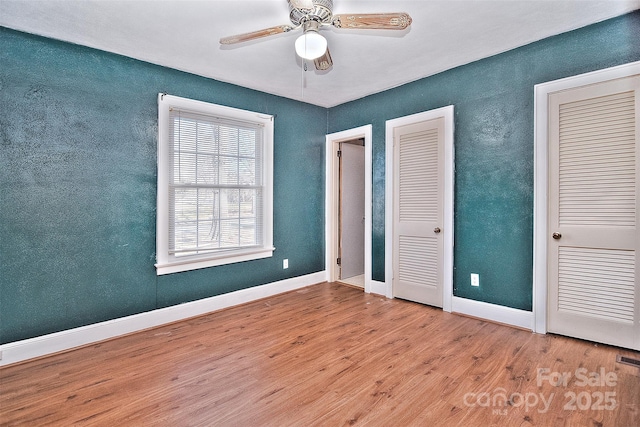 unfurnished bedroom featuring multiple closets, ceiling fan, and light hardwood / wood-style floors