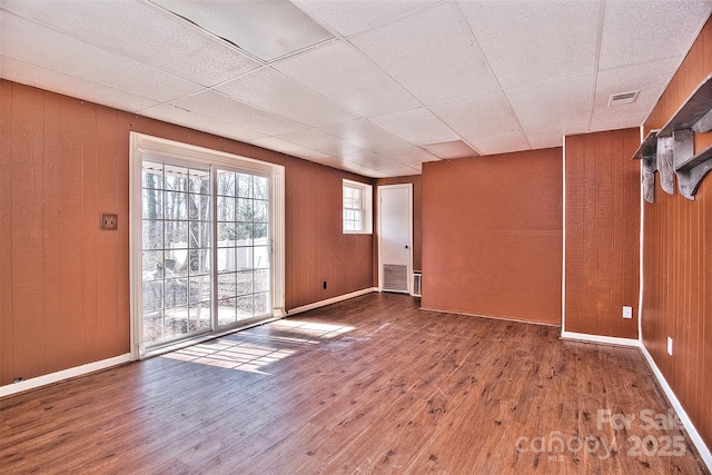 spare room with a drop ceiling, wooden walls, and wood-type flooring