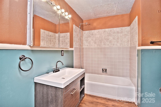 bathroom with tiled shower / bath combo, a textured ceiling, wood-type flooring, and vanity