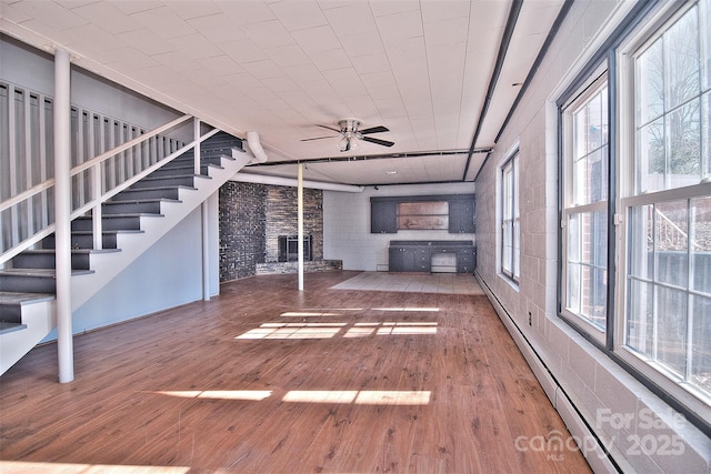 unfurnished living room with ceiling fan, a wealth of natural light, brick wall, and hardwood / wood-style flooring