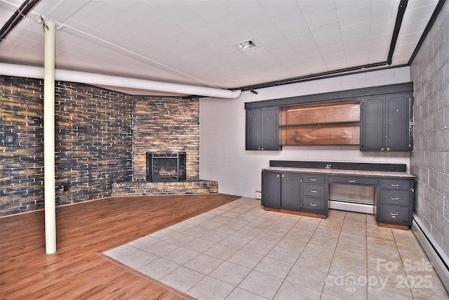 interior space with brick wall, a baseboard radiator, a fireplace, and light hardwood / wood-style floors