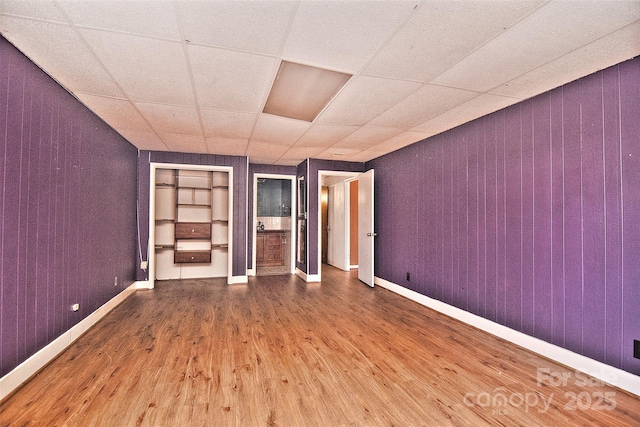 unfurnished bedroom with a paneled ceiling, wooden walls, and hardwood / wood-style flooring