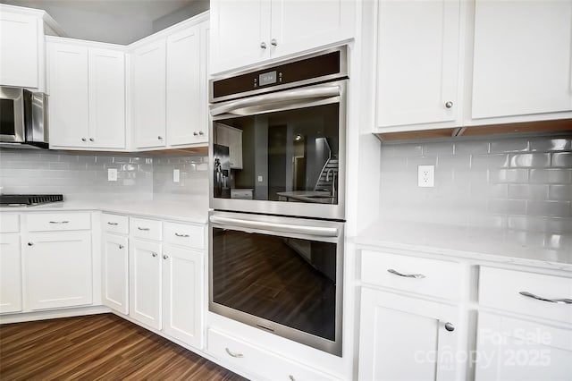 kitchen with stainless steel appliances, backsplash, dark hardwood / wood-style flooring, and white cabinetry