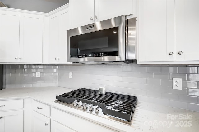 kitchen featuring light stone countertops, stainless steel appliances, white cabinetry, and decorative backsplash