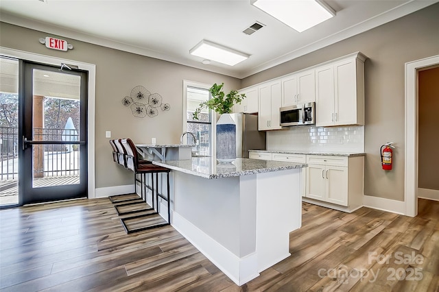 kitchen with light hardwood / wood-style floors, stainless steel appliances, light stone counters, decorative backsplash, and white cabinetry