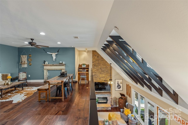 living room featuring dark hardwood / wood-style floors, ceiling fan, a stone fireplace, and lofted ceiling