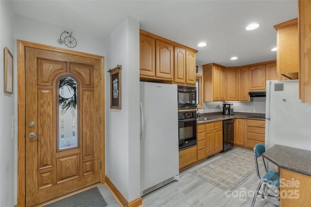 kitchen with dark stone countertops, light hardwood / wood-style flooring, black appliances, and sink