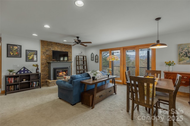 living room featuring ceiling fan, a stone fireplace, and light colored carpet