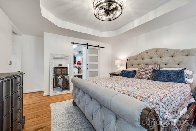 bedroom featuring a raised ceiling, a barn door, and hardwood / wood-style flooring