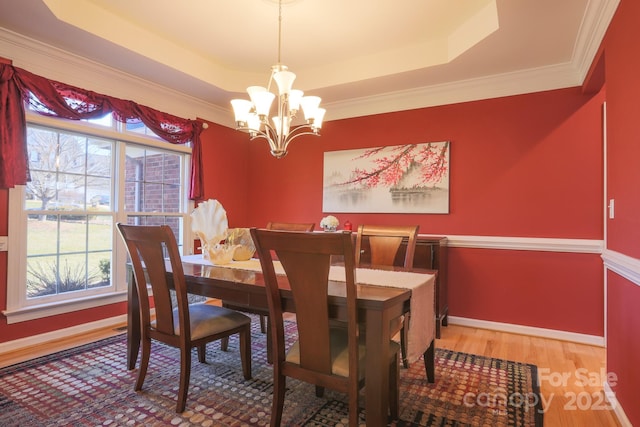 dining room with a raised ceiling, ornamental molding, hardwood / wood-style flooring, and a chandelier