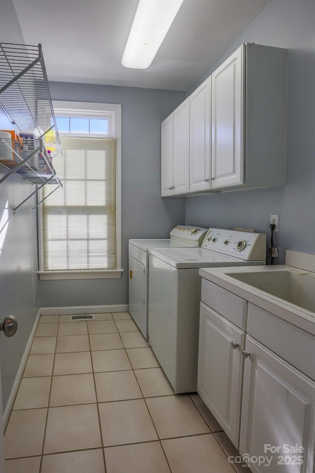 laundry area featuring separate washer and dryer, light tile patterned floors, and cabinets