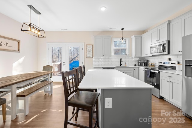 kitchen featuring decorative light fixtures, a kitchen island, sink, stainless steel appliances, and french doors